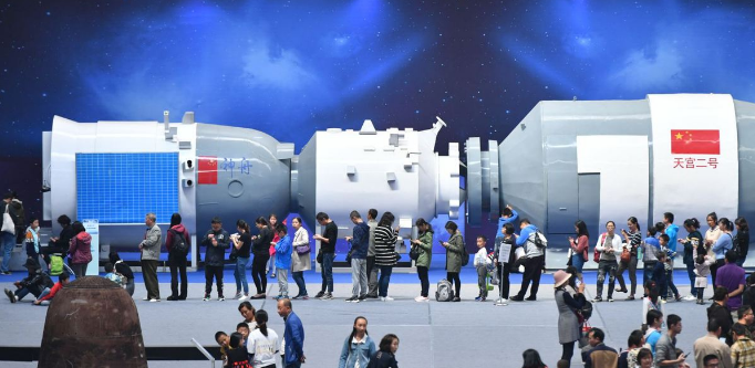 Visitors queue up to try out simulated games in front of a model of Tiangong-2 spacecraft